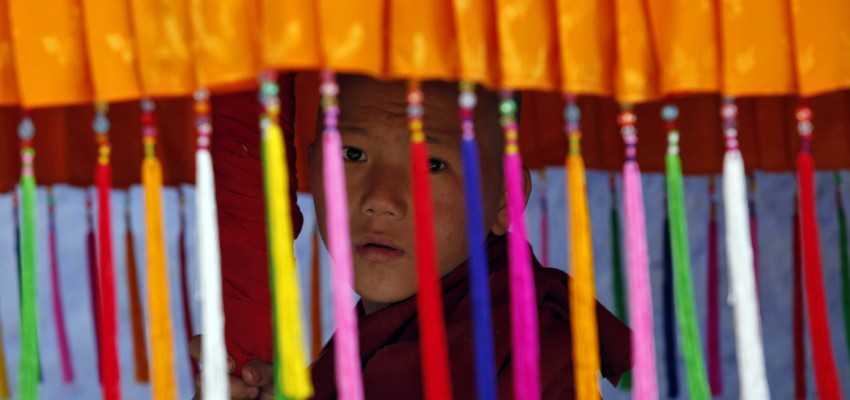 Image: A young monk holds a traditional parasol as he waits for the arrival of Tibet